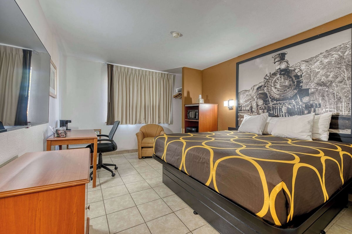 Une chambre d’hôtel avec un lit, un bureau, une chaise, une armoire et un grand tableau encadré au mur.