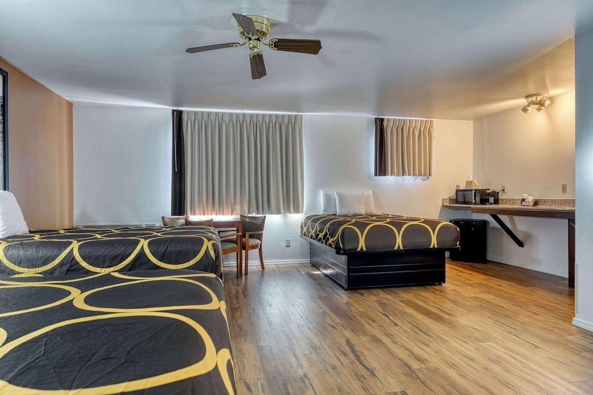 Une chambre d’hôtel avec deux lits, un bureau, une chaise, un ventilateur de plafond et une fenêtre avec des rideaux.