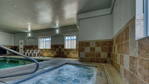 Een wellnessruimte met een bubbelbad, een zwembad en een zithoek met stoelen.