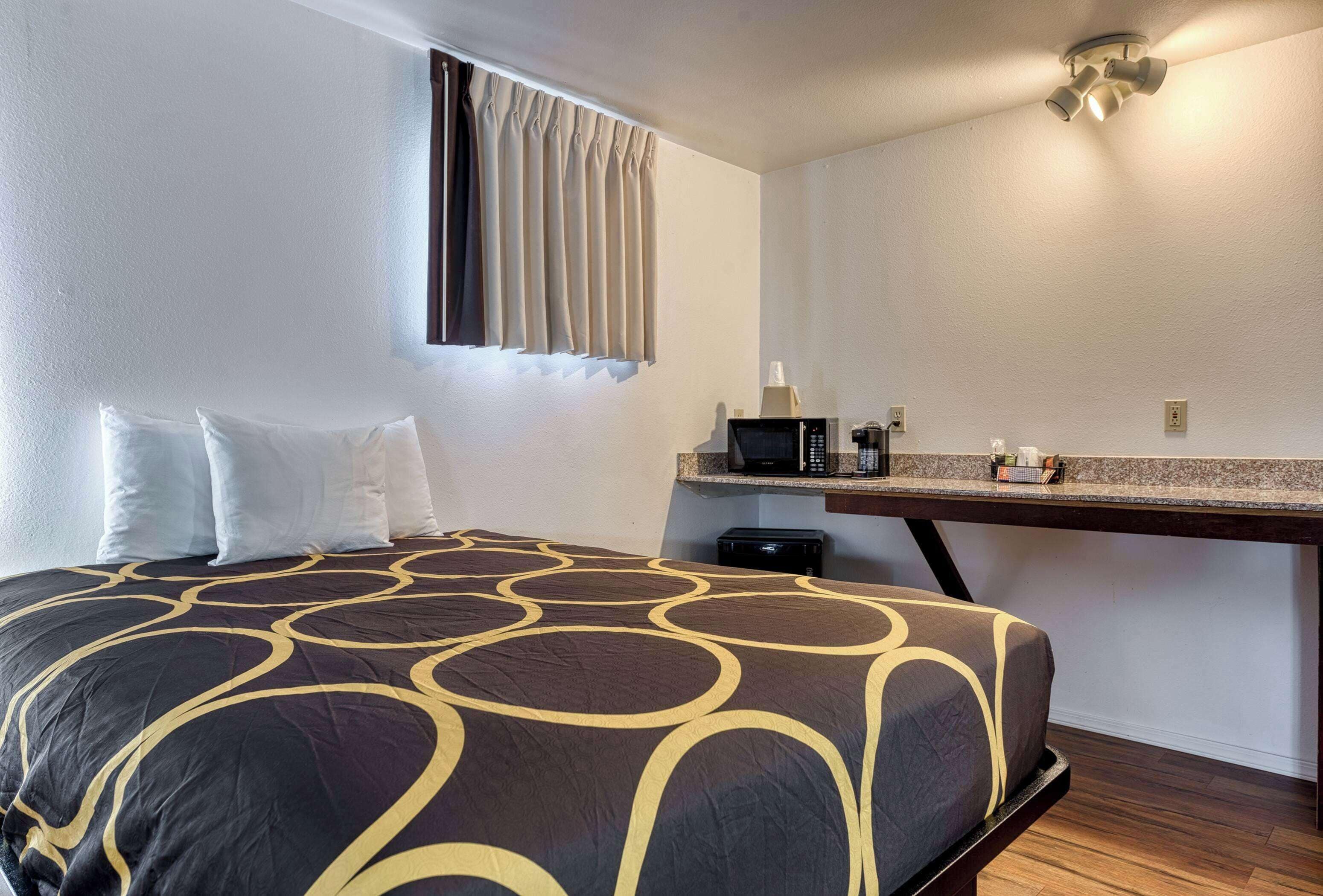 A hotel room with a bed, a small desk with a microwave, and a window with curtains.