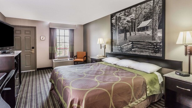 Una habitación de hotel con cama, escritorio, silla, televisor, ventana y un cuadro en la pared.