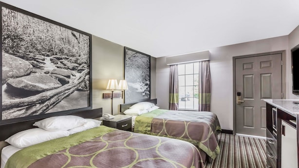 A hotel room with two beds, a desk, a lamp, and a large window with curtains.
