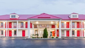 A multi-story hotel with a red roof and white facade, featuring a covered entrance and multiple balconies.