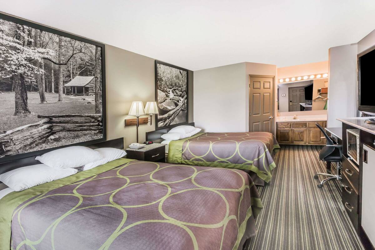 Een hotelkamer met twee bedden, een bureau, een spiegel en een badkamer met een wastafel en spiegel.