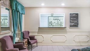 A waiting area with a reception desk, two armchairs, a sofa, teal curtains, a framed welcome sign, and a window with a view of a building.