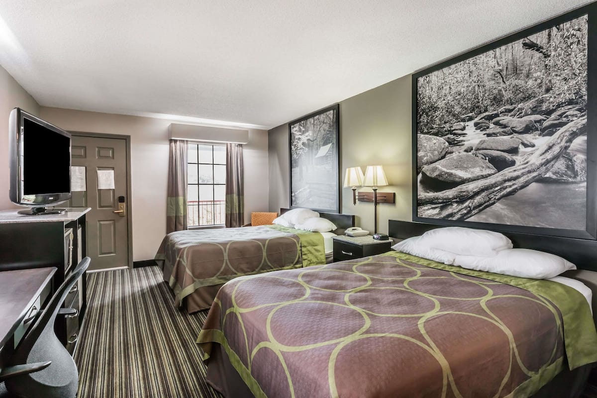 Hotelkamer met twee bedden, een bureau met een televisie, een raam met gordijnen en een groot ingelijst schilderij aan de muur.