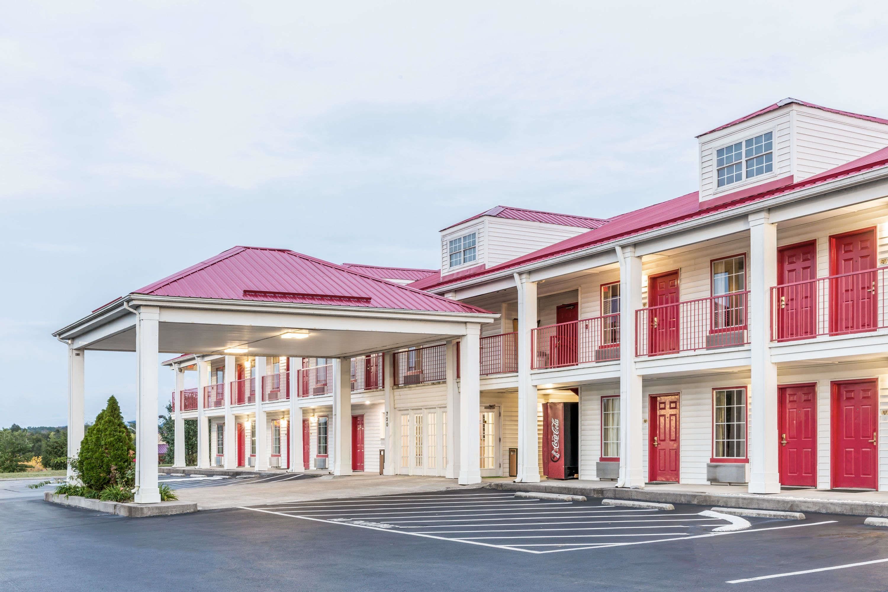 A multi-story motel with red-framed windows and doors, a covered parking area, and a Coca-Cola sign.