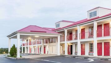 A multi-story motel with red-framed windows and doors, a covered parking area, and a Coca-Cola sign.