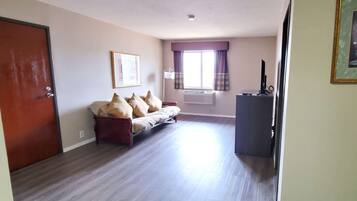 Una habitación con sofá, televisión y ventana con cortinas.