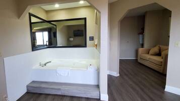A modern bathroom with a large bathtub, a mirror, and a wooden floor.