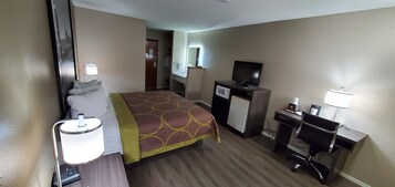 A hotel room with a bed, a desk, a television, a microwave, and a lamp.