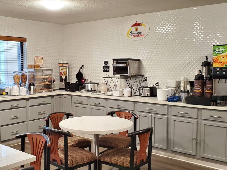 A compact kitchen with a microwave, toaster, and coffee maker. There is a dining table with chairs and a window with blinds.