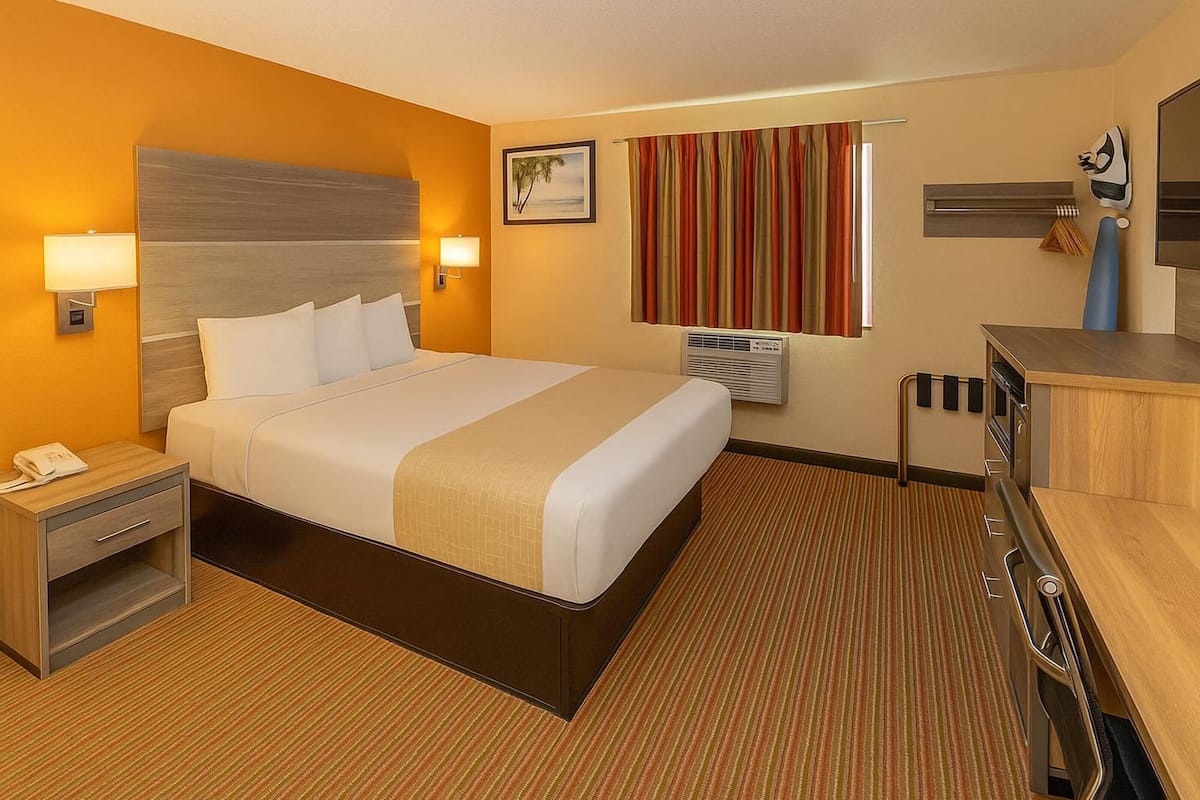 A hotel room with a large bed, bedside lamps, a desk, and an air conditioning unit.