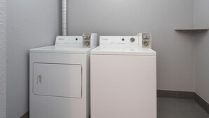 Two front-loading washing machines in a laundry room with a light fixture above and a vent pipe on the left. - Travelodge by Wyndham Muskegon (Muskegon)