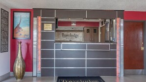 A reception area with a 'Travelodge' sign, a large vase, and a 'See America' poster. - Travelodge by Wyndham Muskegon (Muskegon)