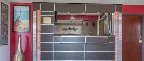 Una zona de recepción con un letrero de 'Travelodge', un jarrón grande y un cartel que dice 'See America'.