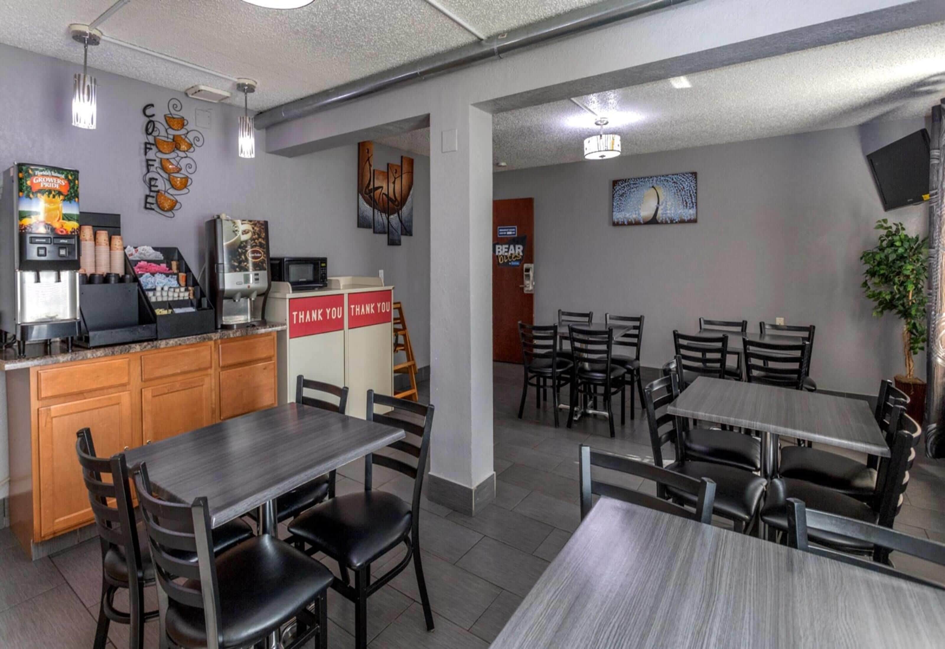Un restaurant avec un comptoir, des machines à café et une pancarte indiquant « Merci ». Des tables et des chaises sont disposées pour accueillir les clients.