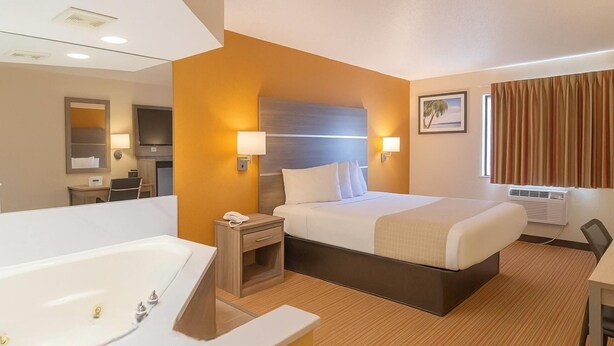A hotel room with a large bed, a separate bathroom with a bathtub, a desk, and a television. - Travelodge by Wyndham Muskegon (Muskegon)