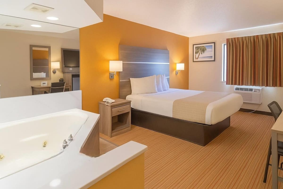 A hotel room with a large bed, a separate bathroom with a bathtub, a desk, and a television.