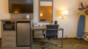 A hotel room with a desk, a television, a microwave, a small refrigerator, a chair, a mirror, a lamp, and a hanging iron. - Travelodge by Wyndham Muskegon (Muskegon)