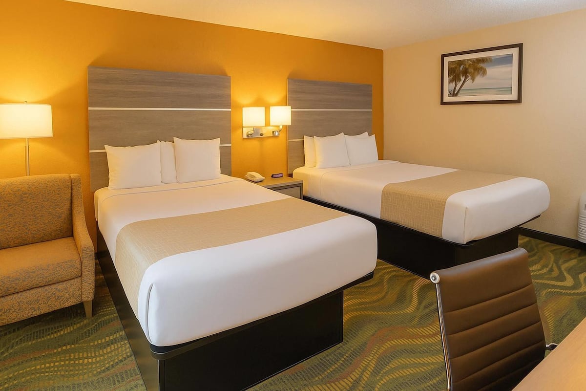 A hotel room with two beds, a sofa, a chair, and a painting on the wall.