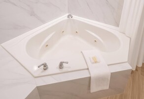 Bañera de esquina con dos llaves y una toalla.