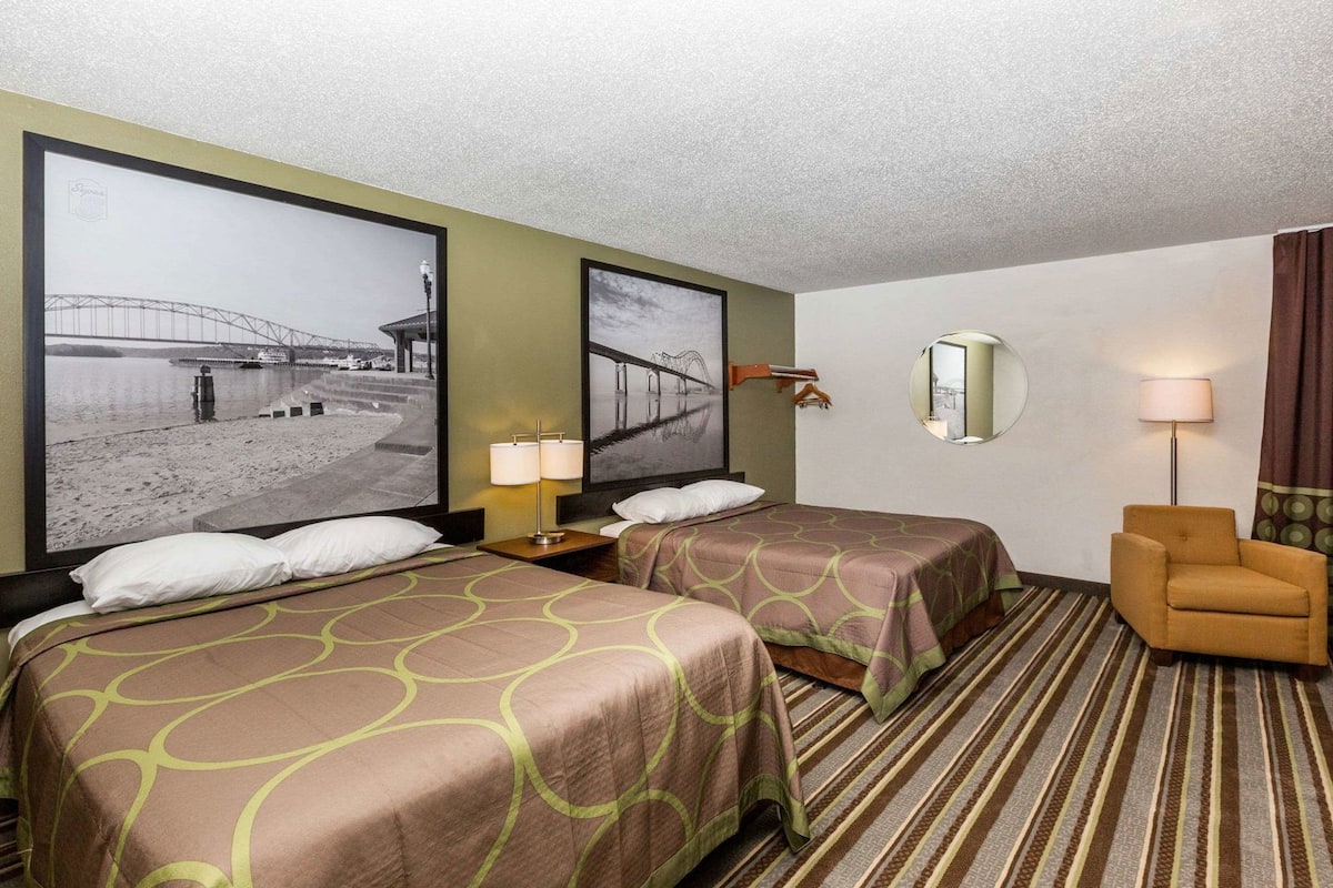 Een hotelkamer met twee bedden, een stoel, een lamp en twee grote foto’s in een lijst van een brug.