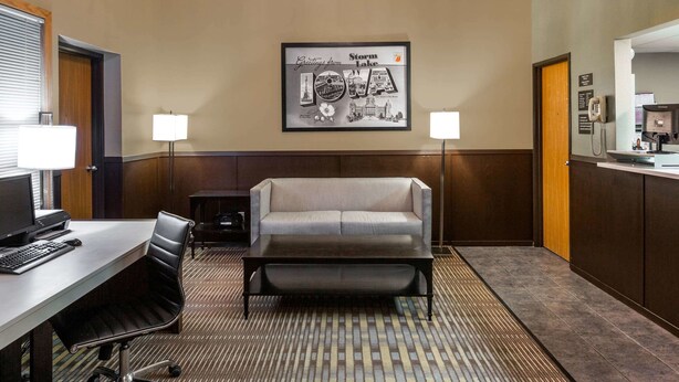 A hotel room with a desk, computer, chair, sofa, and a framed picture of Iowa on the wall.