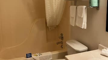 Een badkamer met een badkuip, toilet en wastafel. Handdoekrek met opgevouwen handdoeken en een groene zeepdispenser.