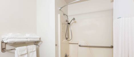 Un baño con bañera, ducha, toallero con toallas dobladas y un taburete pequeño.