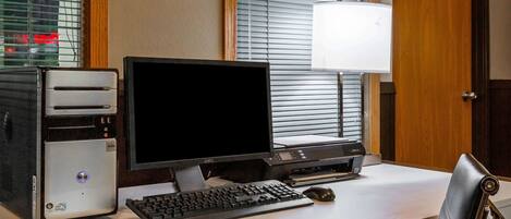 Ein Hotelzimmer mit einem Schreibtisch, auf dem ein Computer, eine Tastatur, eine Maus und eine Lampe stehen.
