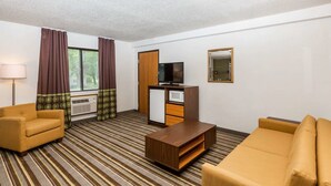 A hotel room with a striped carpet, a sofa, a chair, a TV, a microwave, and a wardrobe.