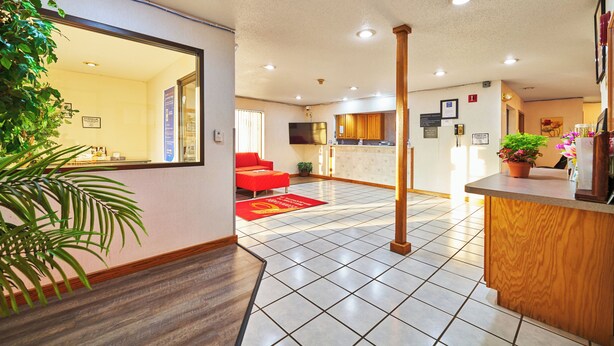 A hotel lobby with a tiled floor, a red sofa, a wooden reception desk, and a large mirror. - Econo Lodge Maquoketa (Maquoketa)