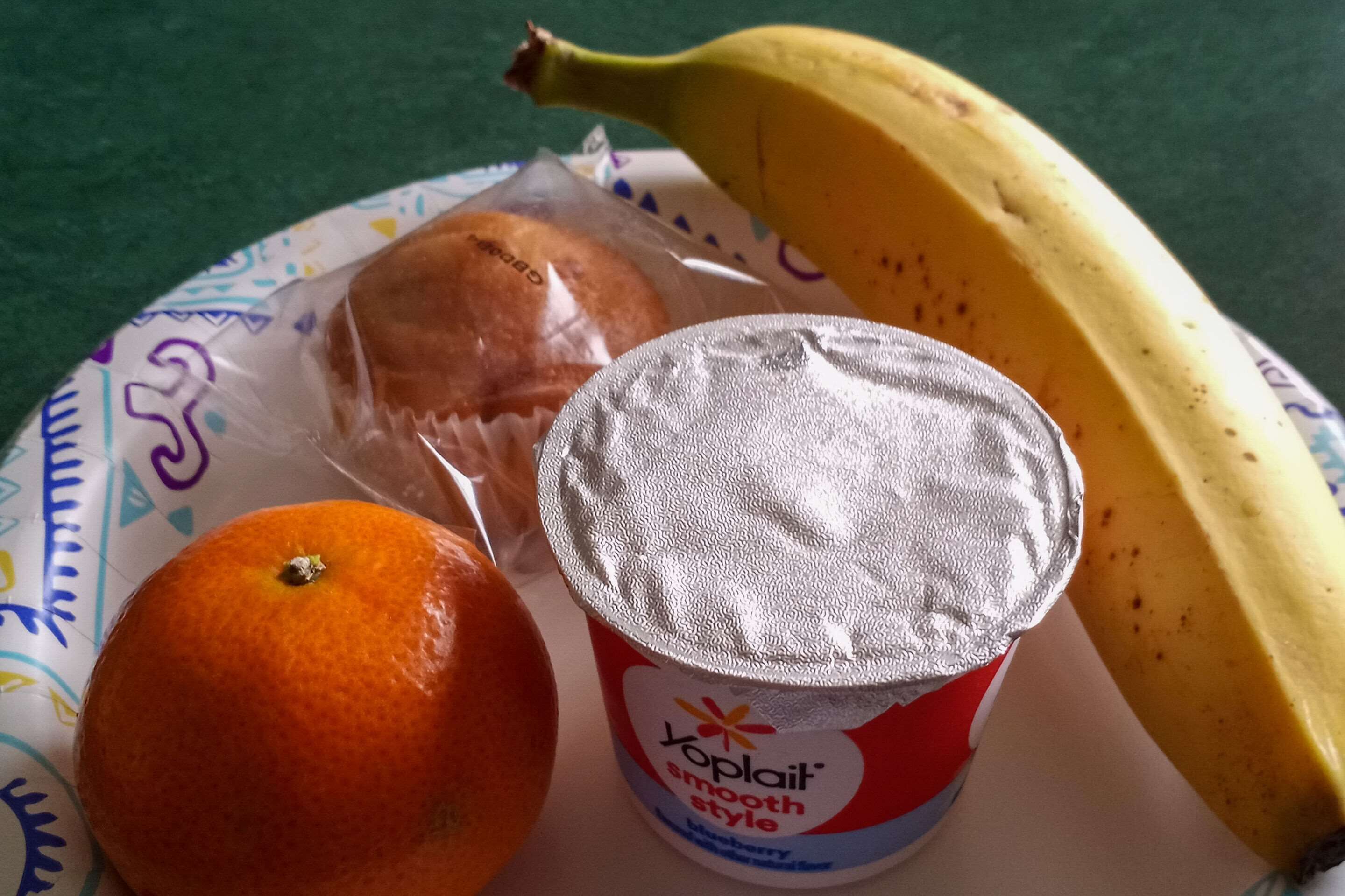 En tallerken med en banan, en appelsin og et yoghurtglas.