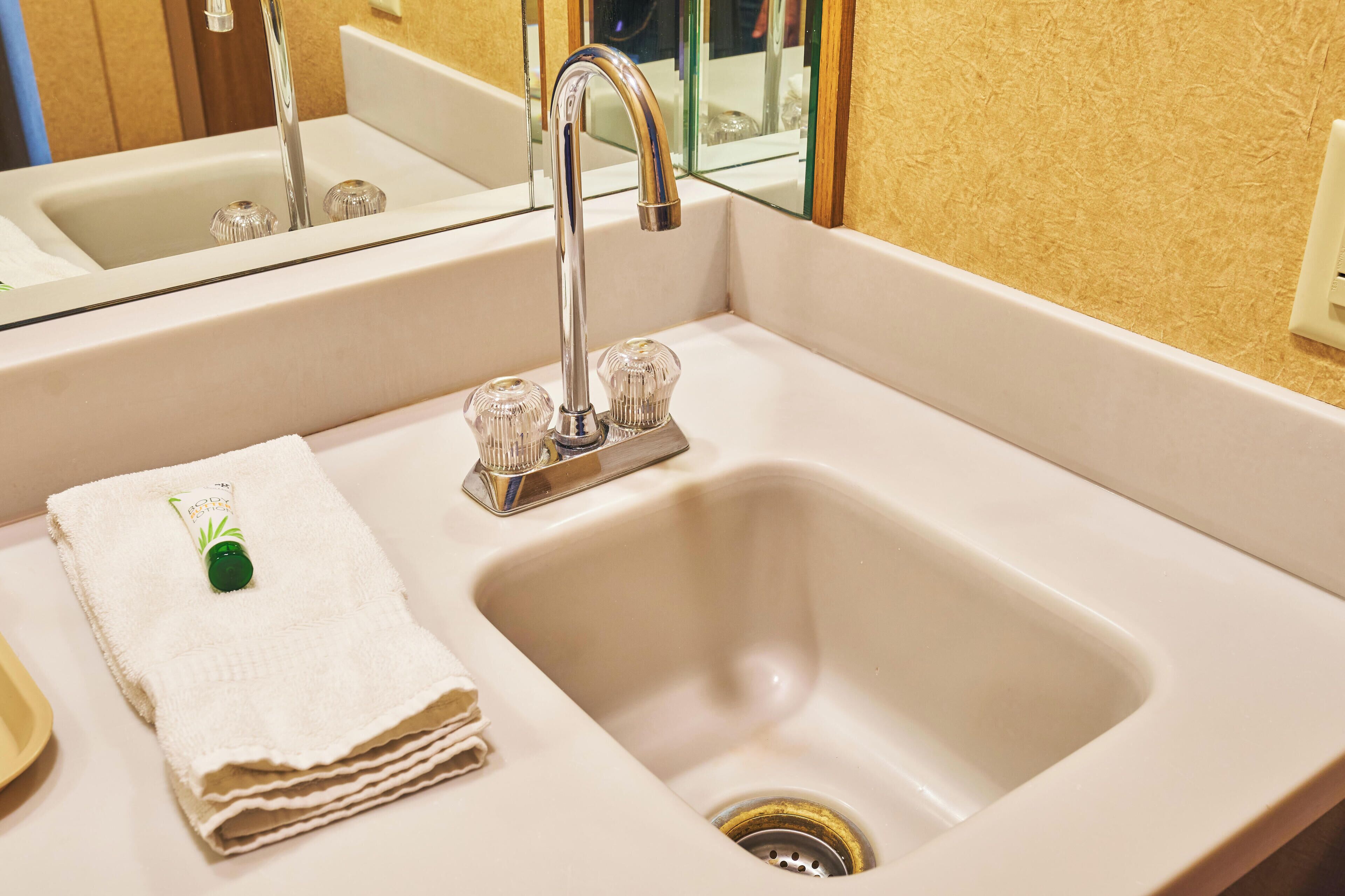 A bathroom sink with a modern faucet, a mirror above it, and a towel with a green bottle on it.
