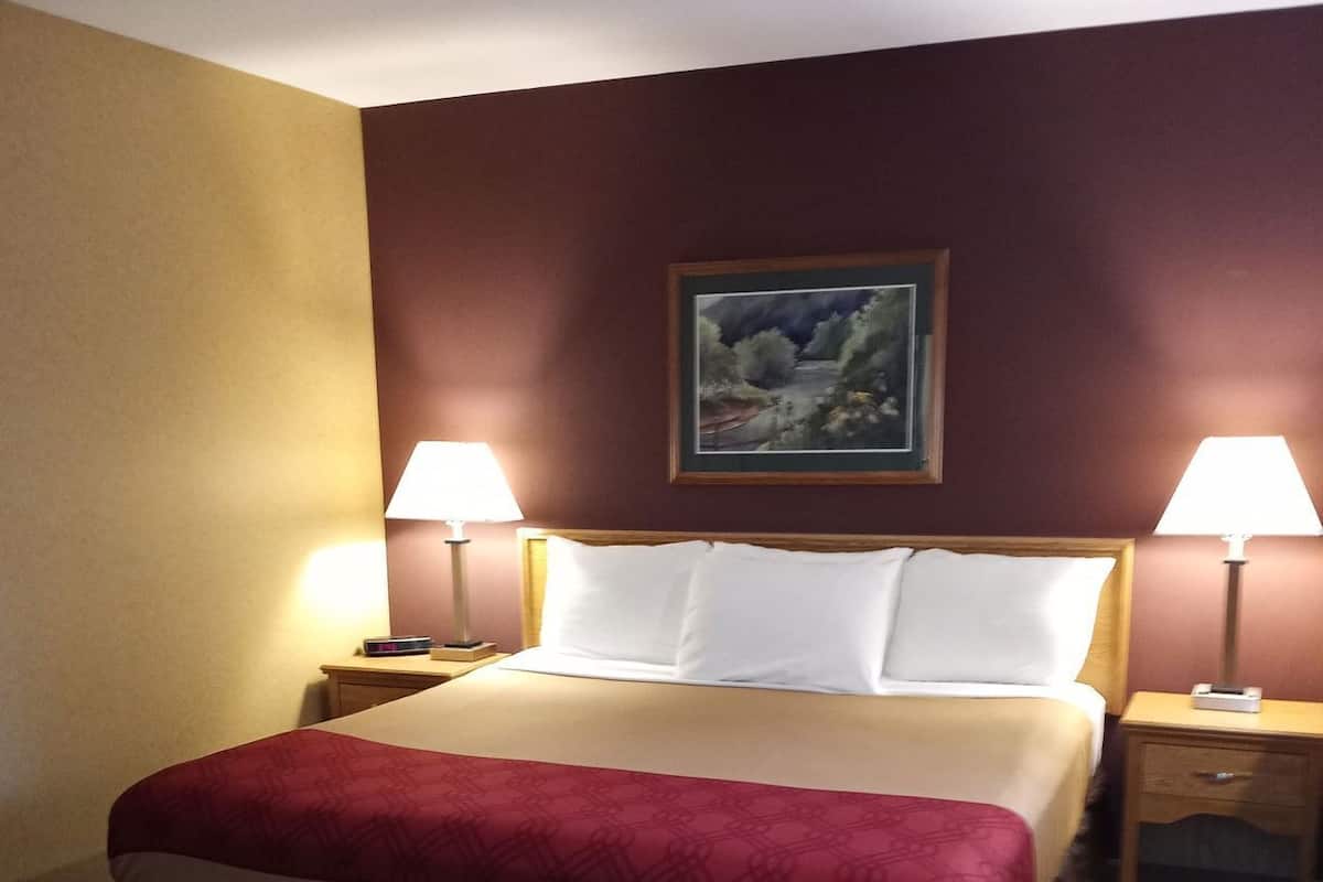 Una habitación de hotel con una cama grande, dos mesitas de noche y un cuadro en la pared.