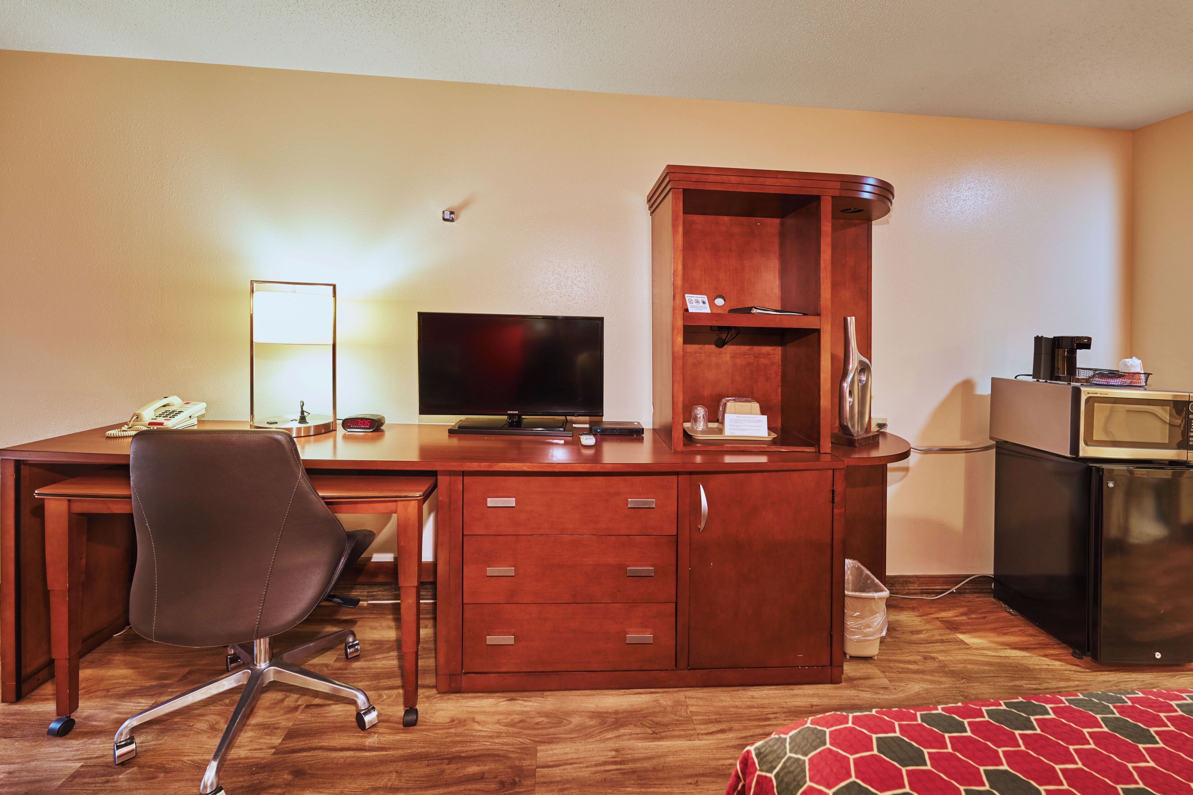 Una habitación de hotel con un escritorio de madera, un televisor, un microondas y una pequeña kitchenette.