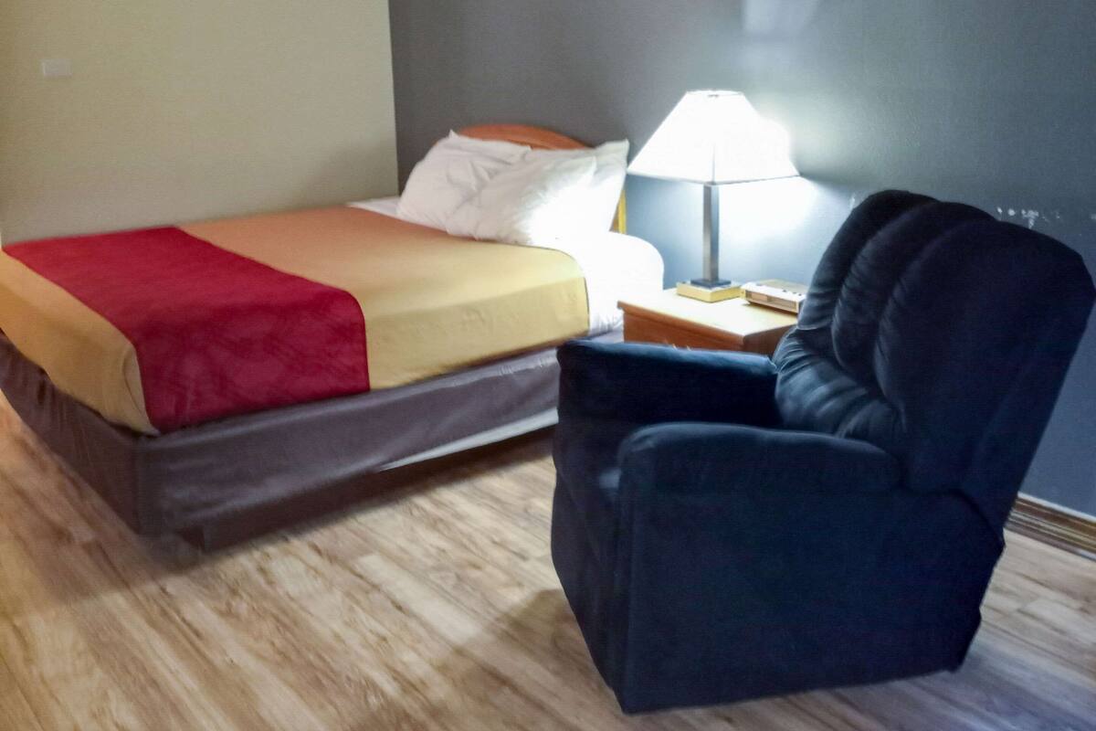 Una habitación de hotel con una cama, una silla, una mesita de noche y una lámpara.