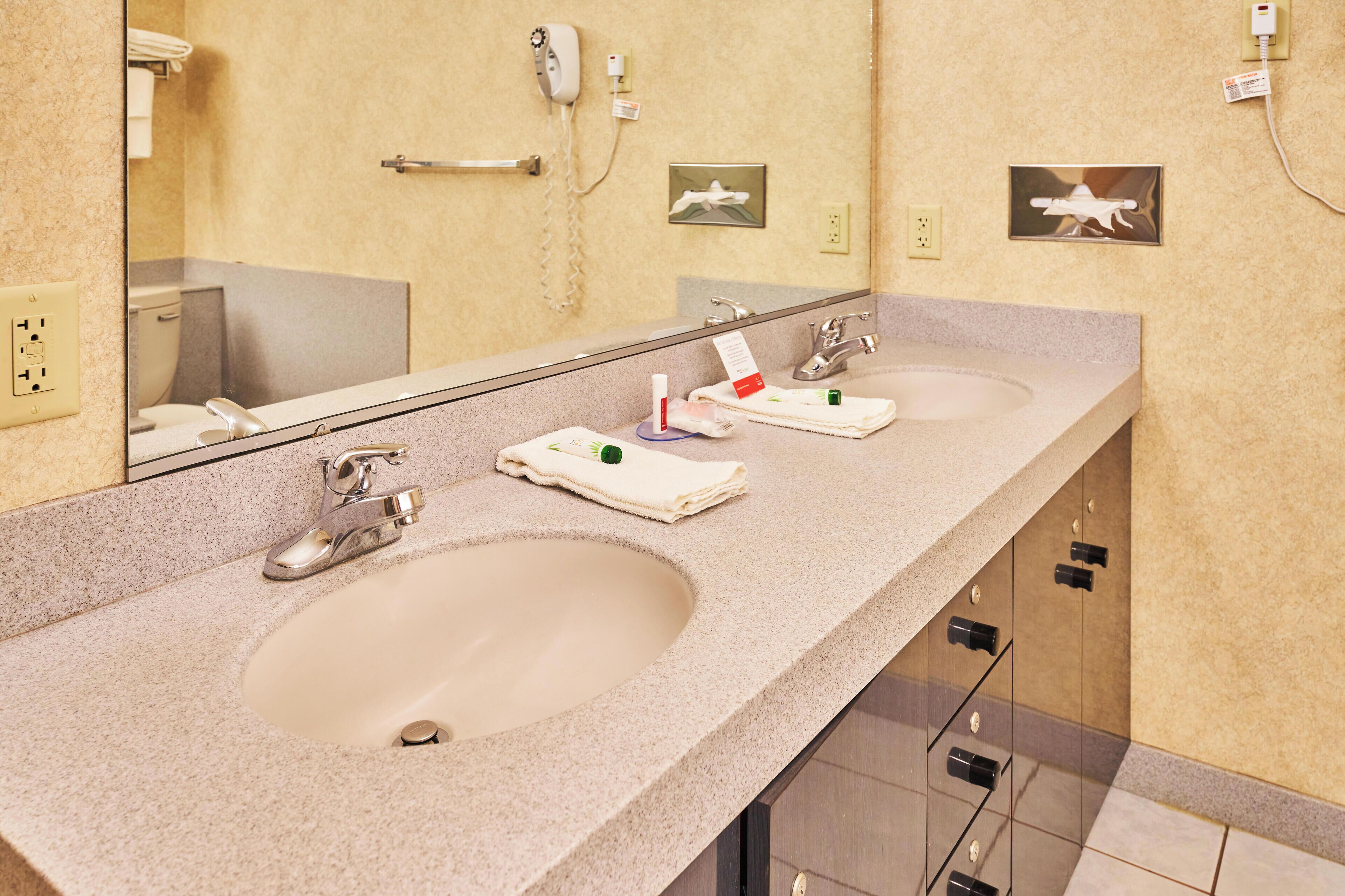 A hotel bathroom with two sinks, a large mirror, and a towel rack.