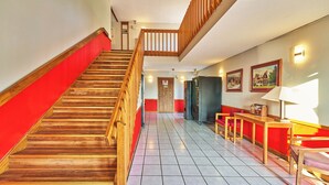 A staircase with wooden steps and a red carpet, leading to a second-floor landing with a wooden railing. - Econo Lodge Maquoketa (Maquoketa)