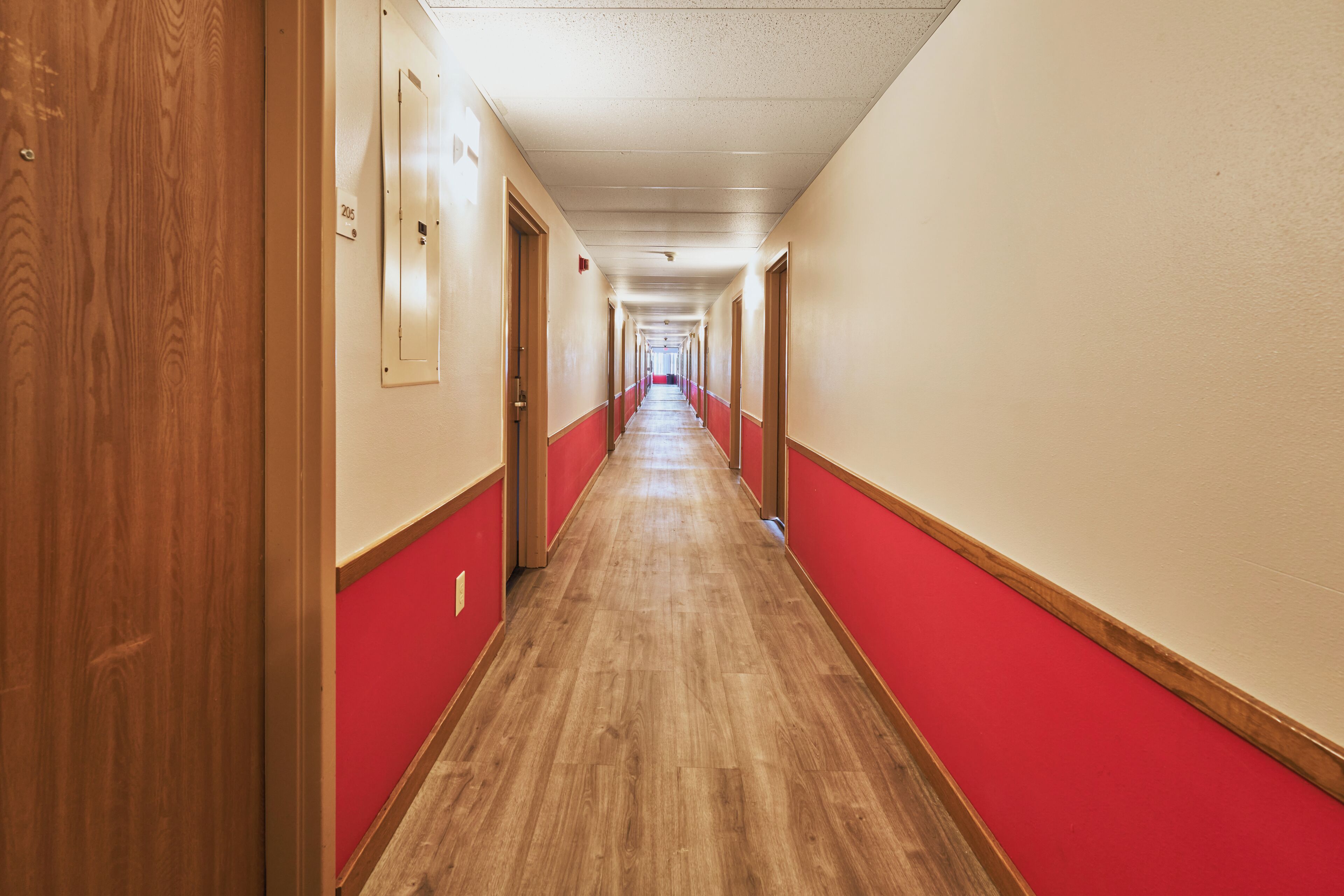 Un pasillo largo y estrecho con puertas de madera a un lado y paredes rojas al otro.