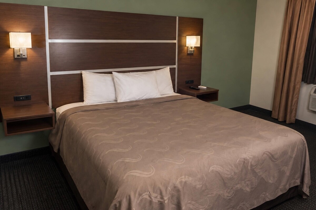 Une chambre d’hôtel avec un grand lit, deux tables de chevet, une tête de lit et des lampes fixées au mur.