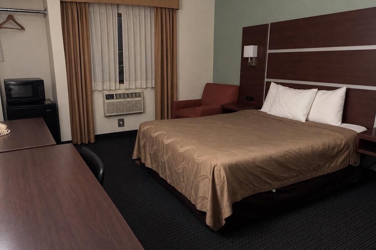 Une chambre d’hôtel avec un lit, un bureau, une chaise, une télévision et une fenêtre avec des rideaux.