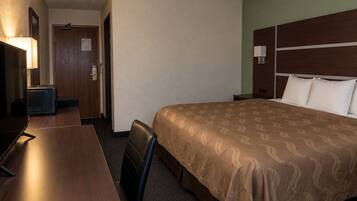 Habitación de hotel con cama, escritorio, silla, lámpara y puerta.