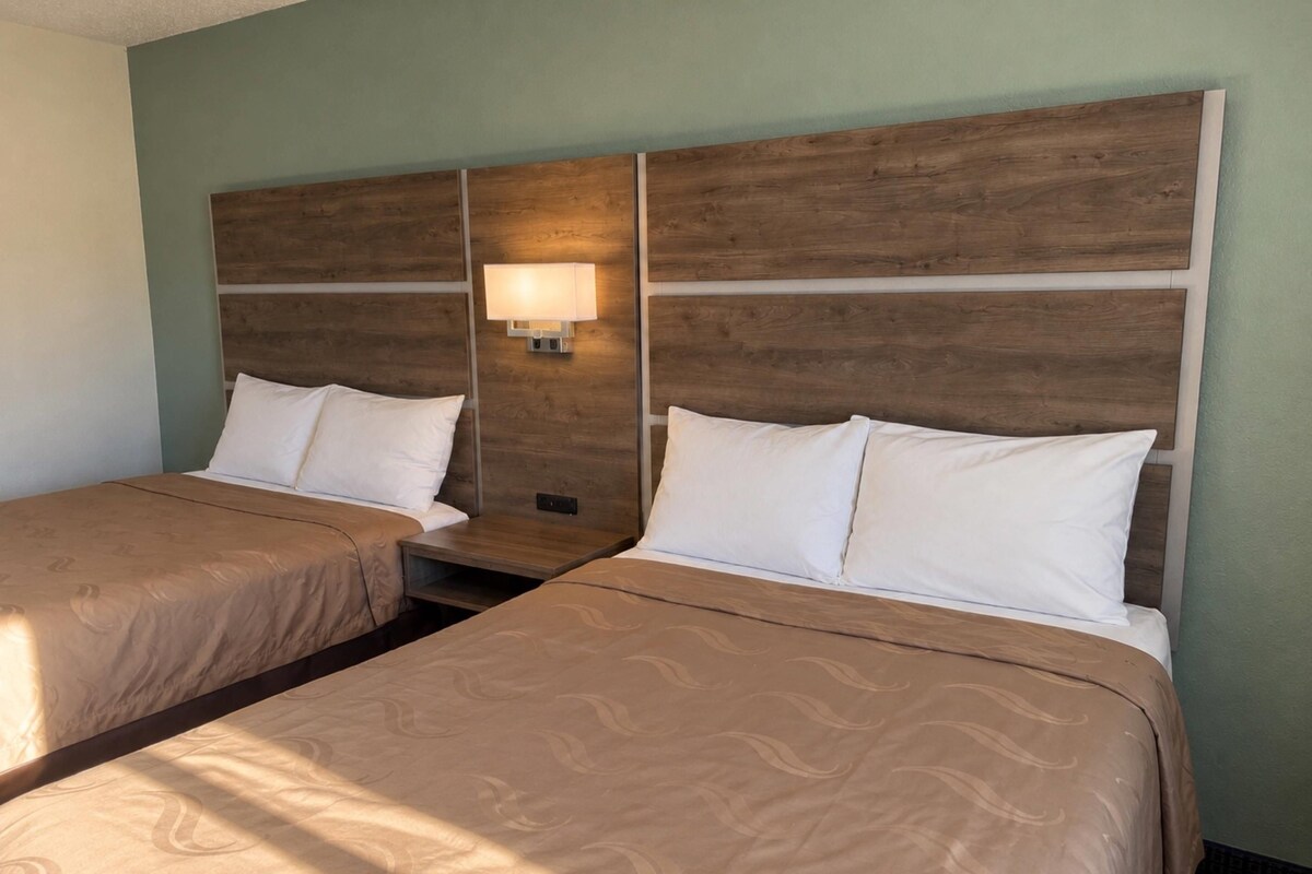 Une chambre d’hôtel avec deux lits, chacun doté d’une tête de lit en bois et de linge de lit blanc.