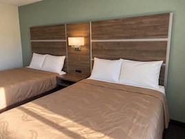 Habitación de hotel con dos camas, cada una con cabecero de madera y ropa de cama blanca.