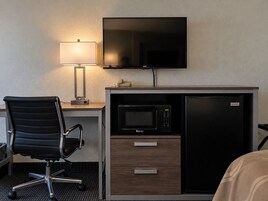 Una habitación de hotel con escritorio, silla, televisión, microondas y refrigerador.