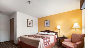 Habitación de hotel con cama, una silla, una mesita de noche y dos lámparas de pared.