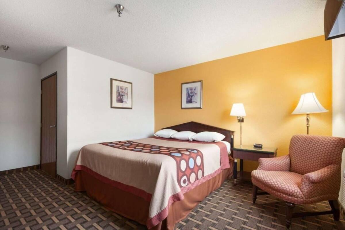 A hotel room with a bed, a chair, a nightstand, and two wall-mounted lamps.