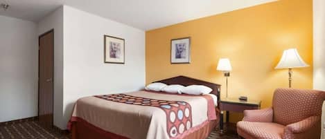 Habitación de hotel con cama, una silla, una mesita de noche y dos lámparas de pared.